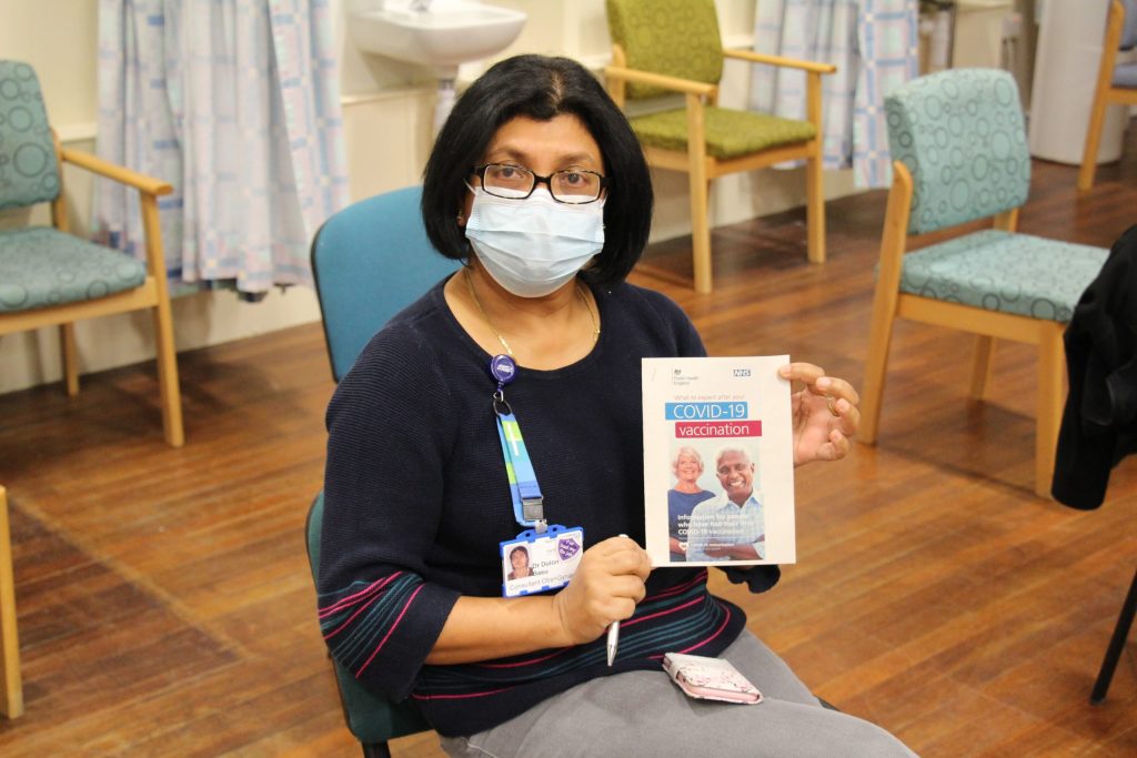 Dolon Basu holds an information leaflet. It reads: "What to expect after your COVID-19 vaccination".