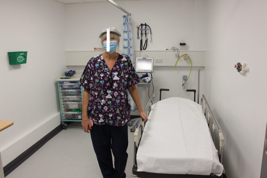 A nurse stands next to a patient bed.