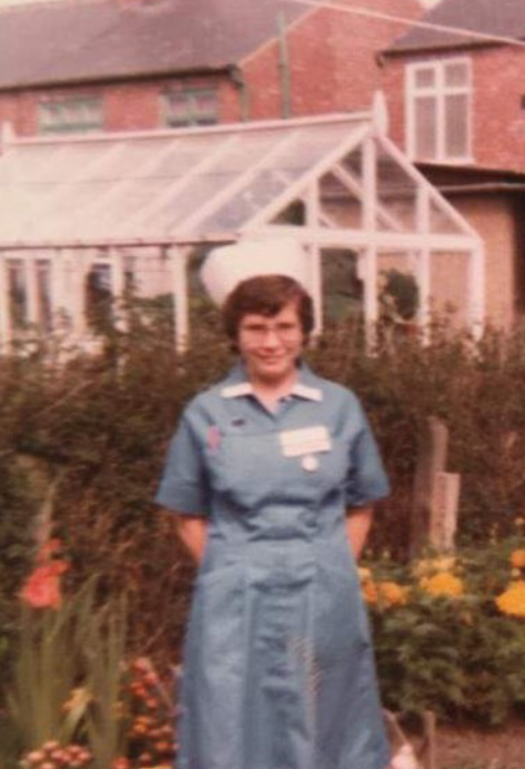 A photo of Amanda when she was younger. She stands in a garden in her nurse's uniform.