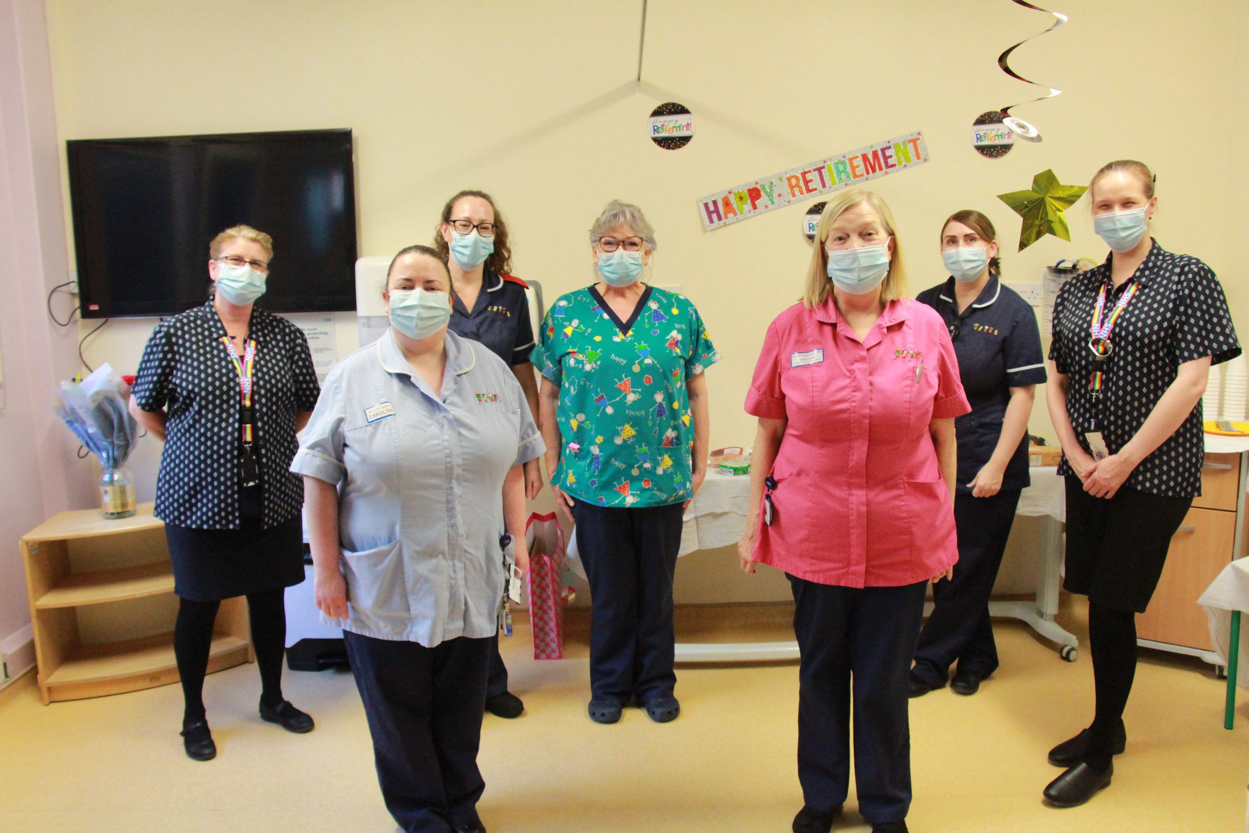 Clare and her colleagues on the children's ward. They stand in front of decorations which read "happy retirement". They all wear face masks.