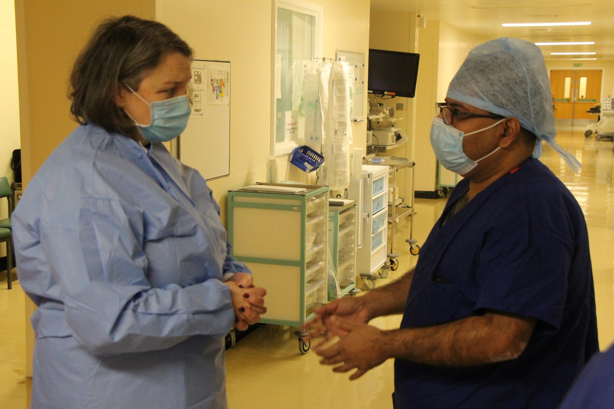 Jill Mortimer speaking to a member of staff in the theatres department. They both wear scrubs and face masks.