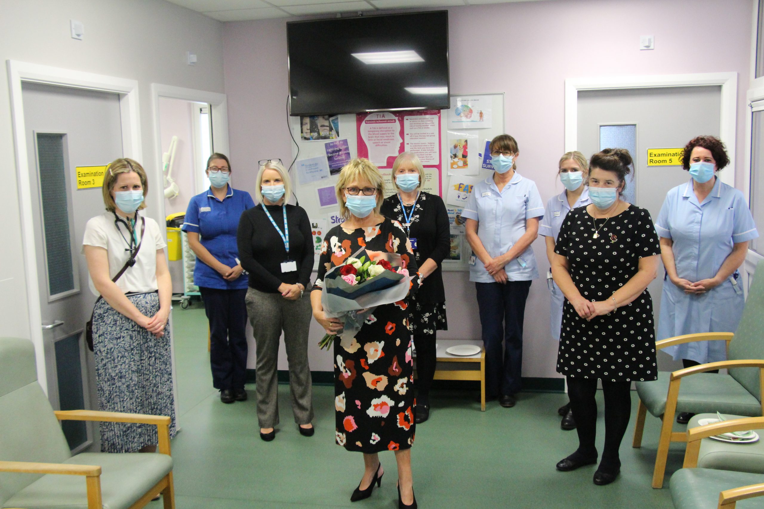 Marian stands with her former colleagues in the ward. She is holding a bunch of flowers. They all wear face masks.