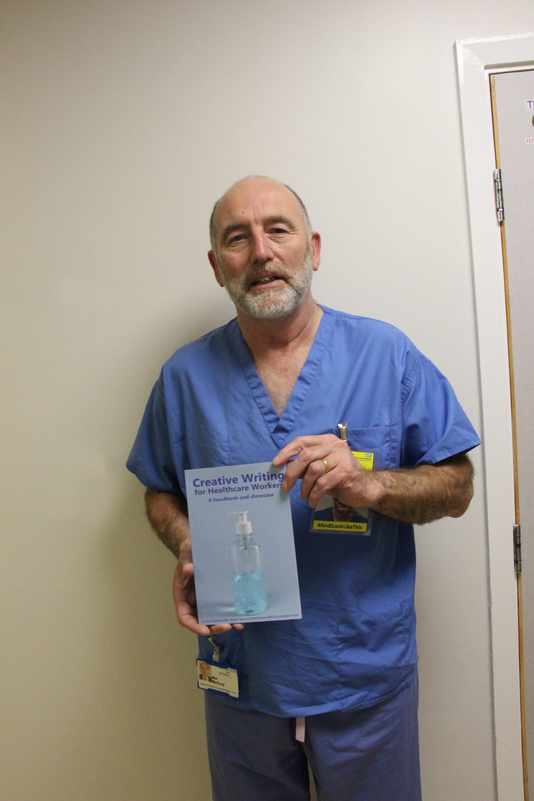 Mel Mcevoy holding a copy of the book. The book features a bottle of hand gel. The title reads: “Creative Writing for Healthcare Workers: A handbook and showcase”.