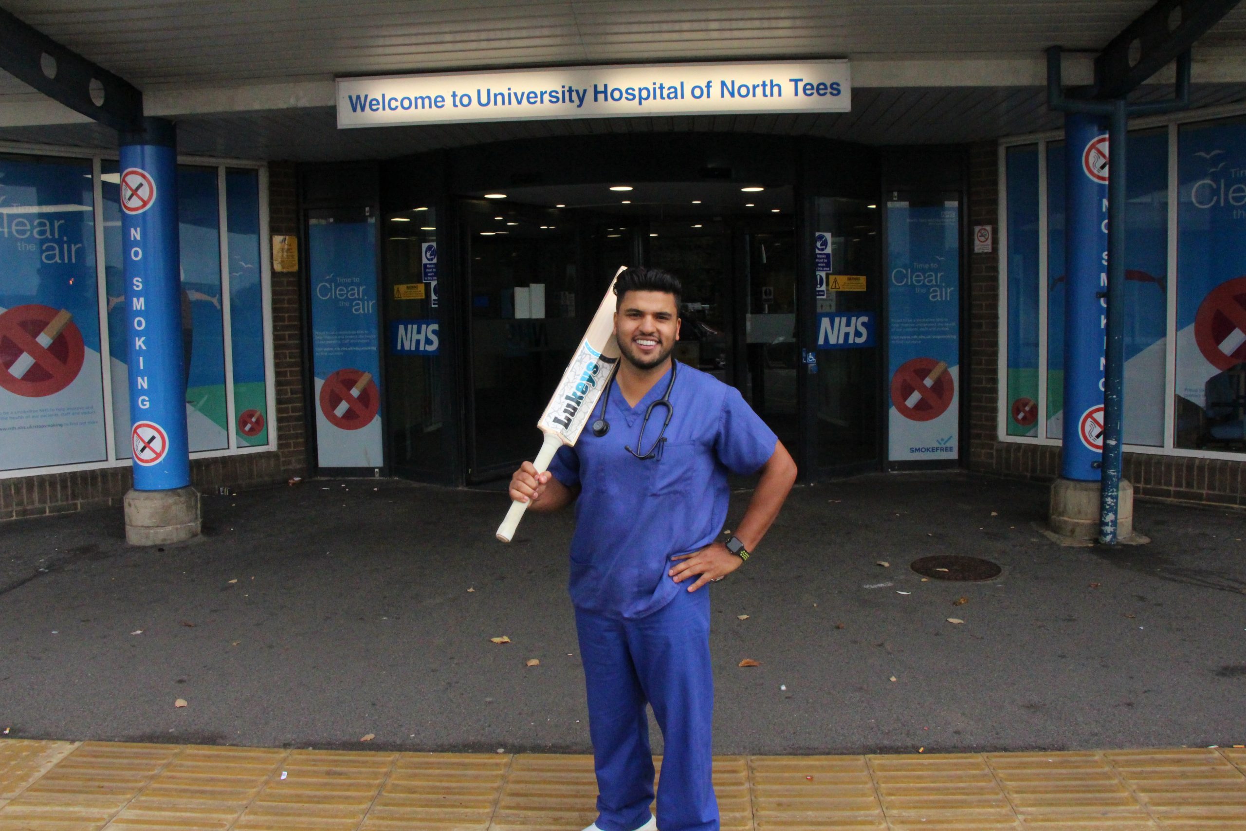 Vishal outside the University Hospital of North Tees. He is holding a cricket bat.