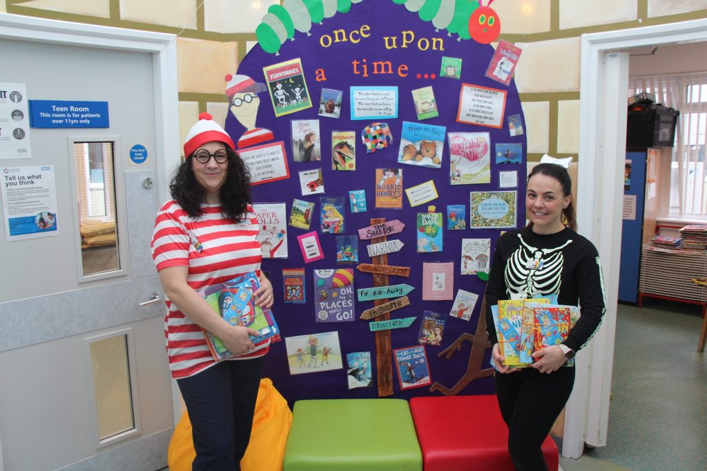 Play specialists dressed as book characters during World Book Day. They are holding books to give as gifts.