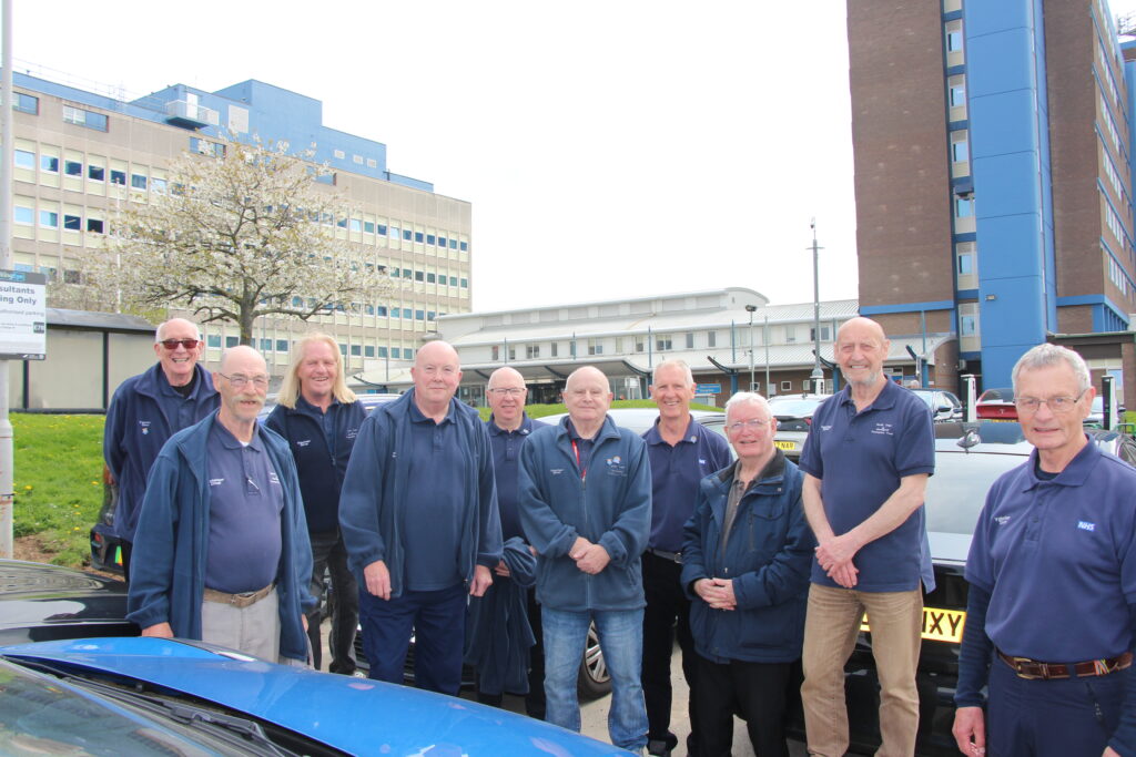 A group of volunteer drivers stand beside a car.