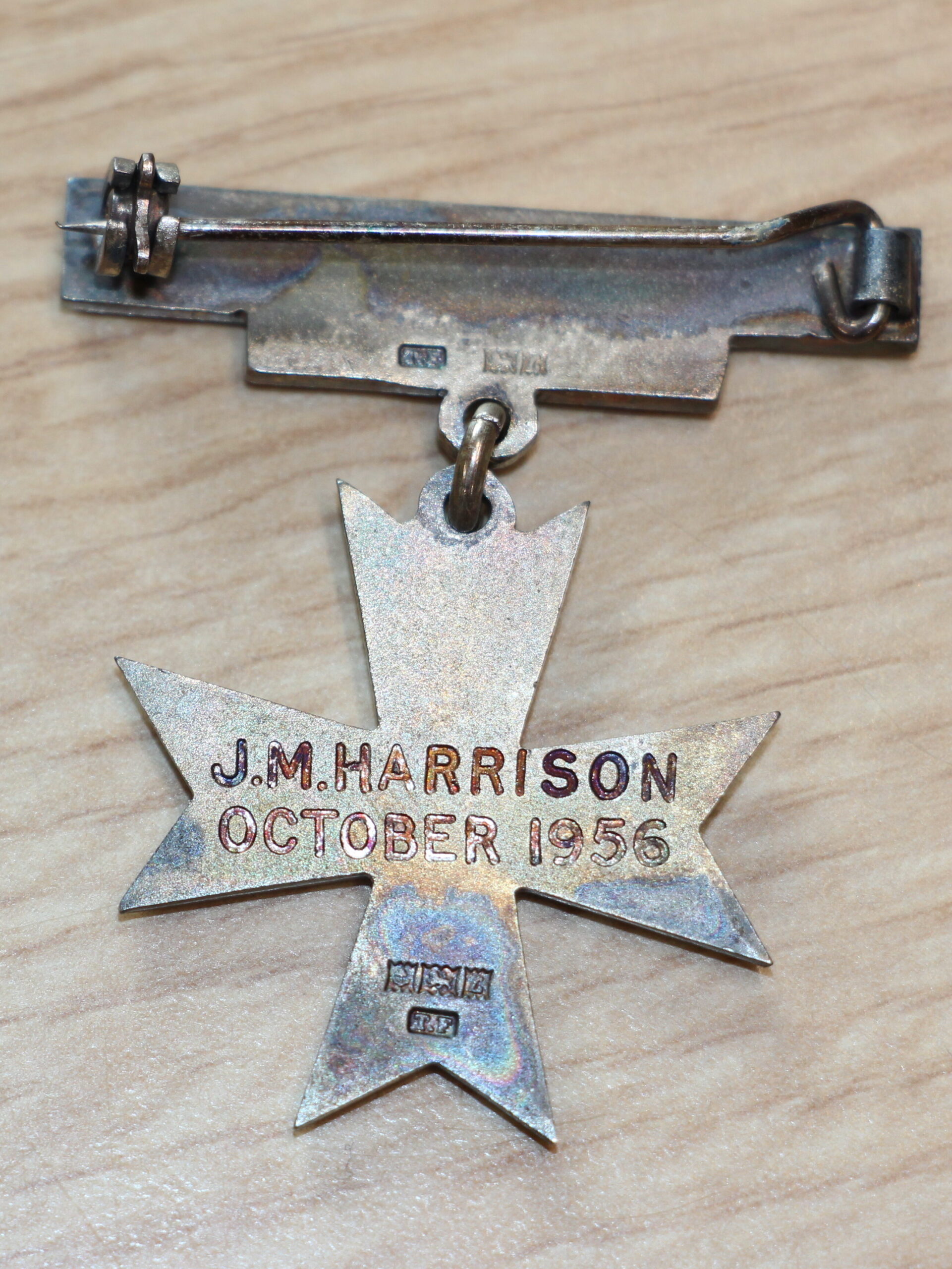 Back of a cross-shaped badge. An engravement reads: "J.M.Harrison October 1956".