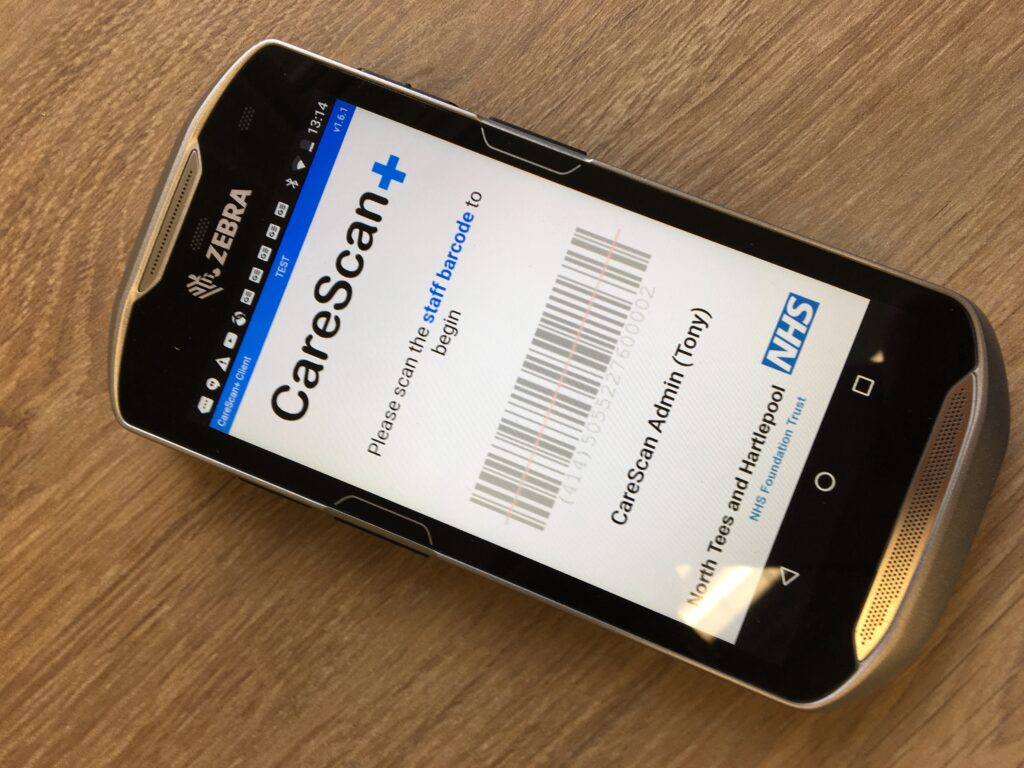 A CareScan+ hand held scanner. A barcode is displayed on the screen,