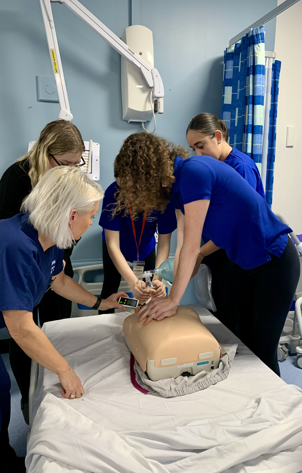 Education trainer assists students with how to perform CPR