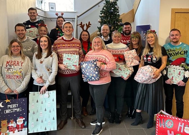 Miller Homes staff hold gifts. They stand in front of a Christmas tree.