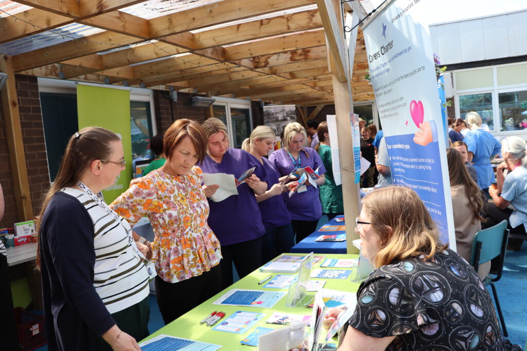 Two staff speak with a stallholder. Staff can be seen in the background reading leaflets.