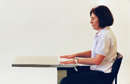Hands resting on a table close to the persons body.