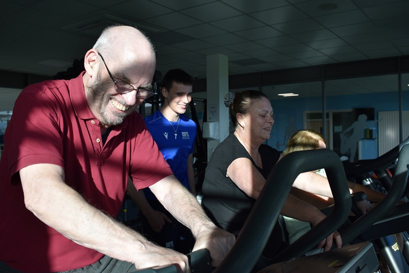 Two people on exercise bikes. A student stands behind them.