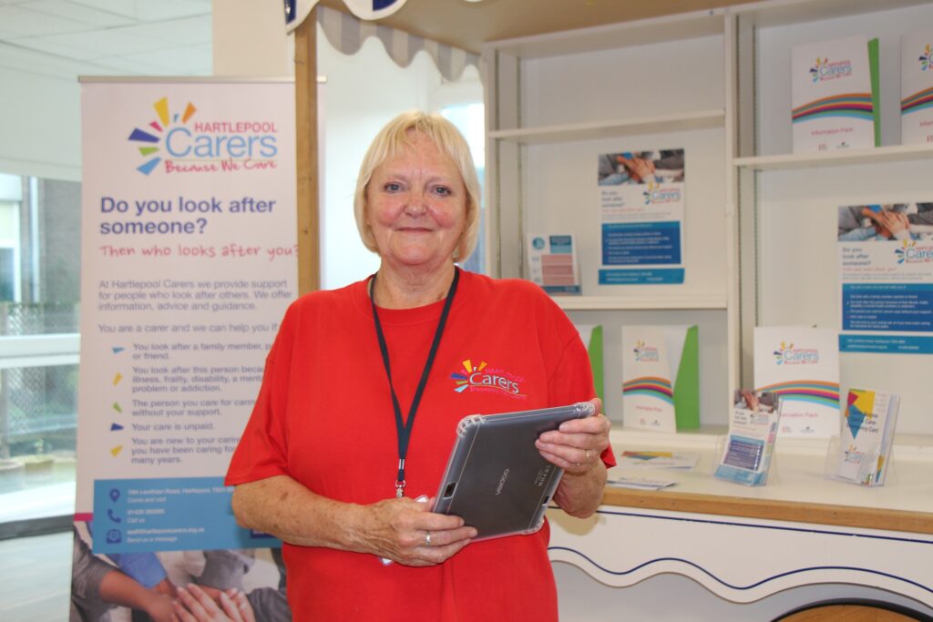 A lady stands in front of a stall. A banner reads 'Hartlepool Carers. Do you look after someone?'
