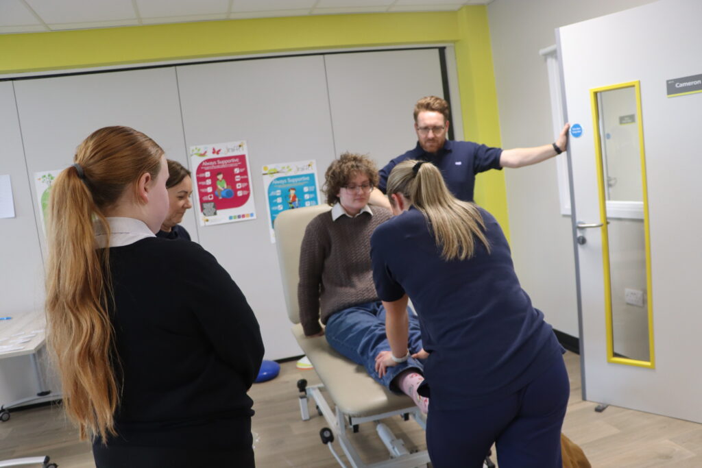 A person receiving physiotherapy on their leg. Two teenage girls watch.