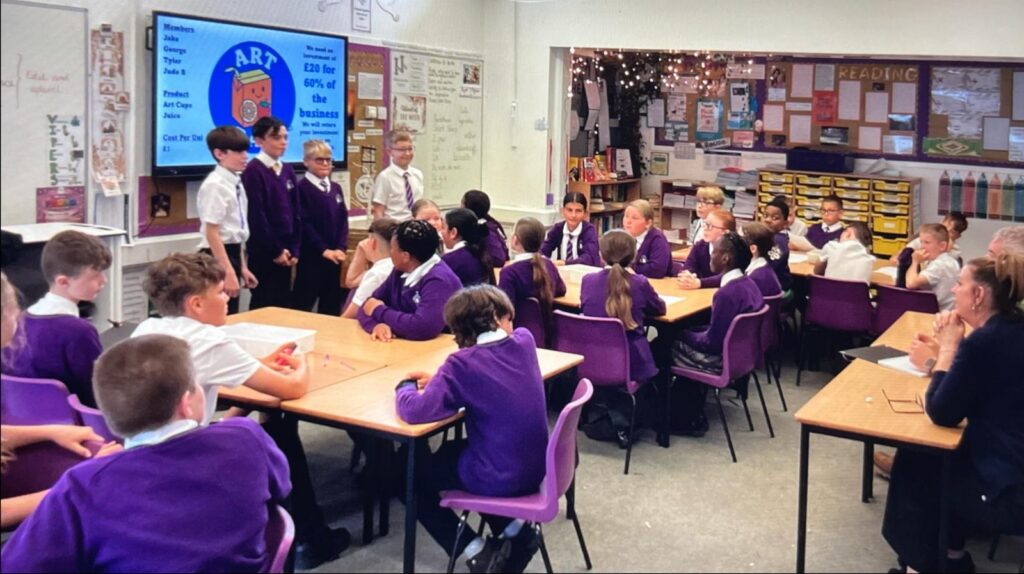 A classroom. Pupils look at a screen which details enterprise day projects.