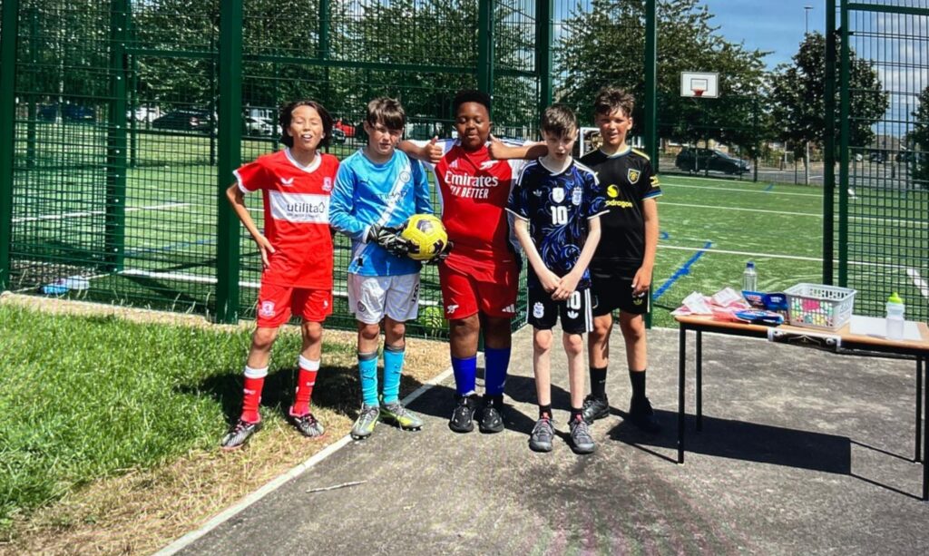 Children wearing football kits. One holds a football.