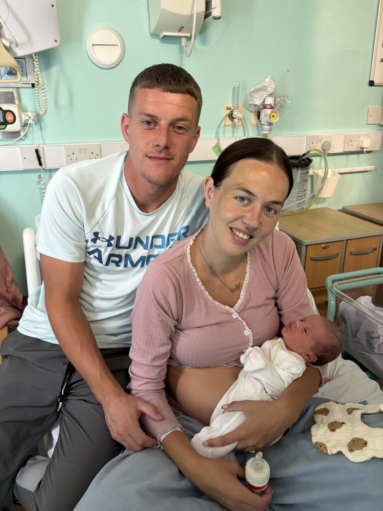 Parents with newborn baby sitting on bedside.