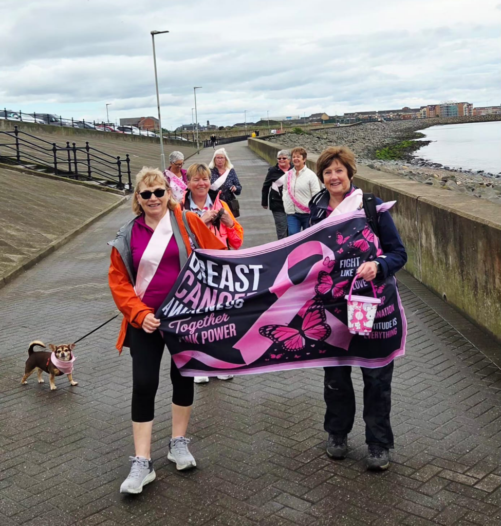 A group of women and a dog walking on the seafront.