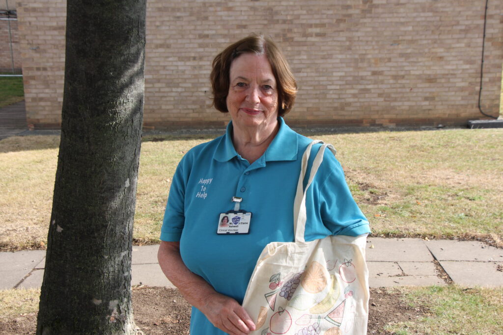 A volunteer carries a tote bag. The bag features an illustrated drawing of various fruit and vegetables.
