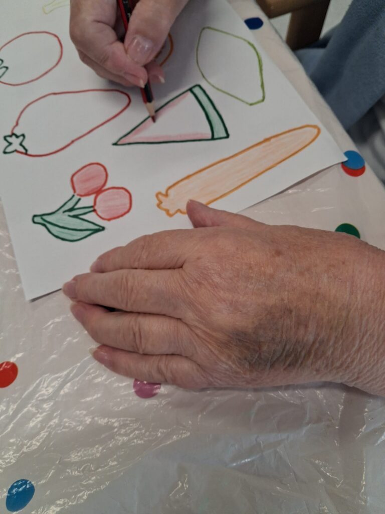A close up an elderly person's hands drawing fruit and vegetables,