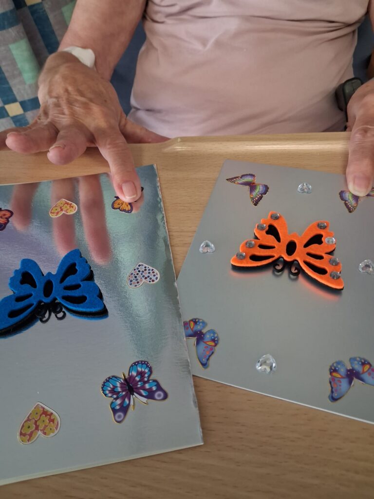 A pair of elderly hands, resting on two homemade cards. The cards have butterflies on them.