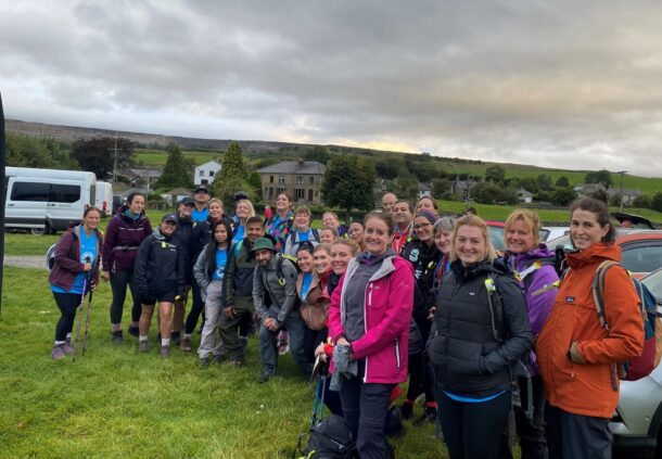A group of people stand in a field. They wear hiking clothing.