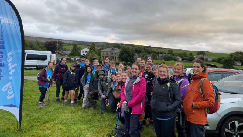 A group of people stand in a field. They wear hiking clothing.