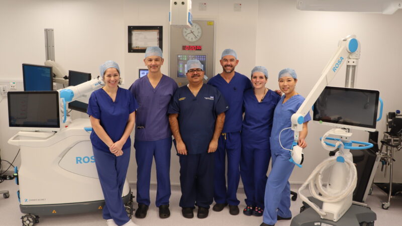Theatre team stood in operating theatre beside a robot.