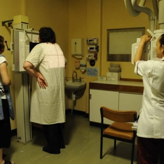 patient stands at x-ray machine with carer while staff member takes x-ray