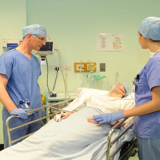Patient is brough around by two theatre staff in theatre recovery room