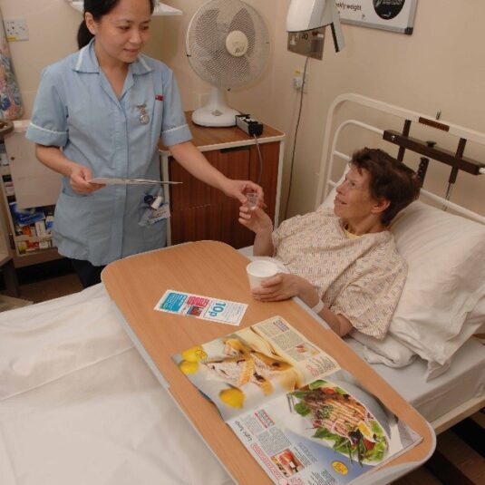 Nurse gives patient a drink and pain medication in ward bed