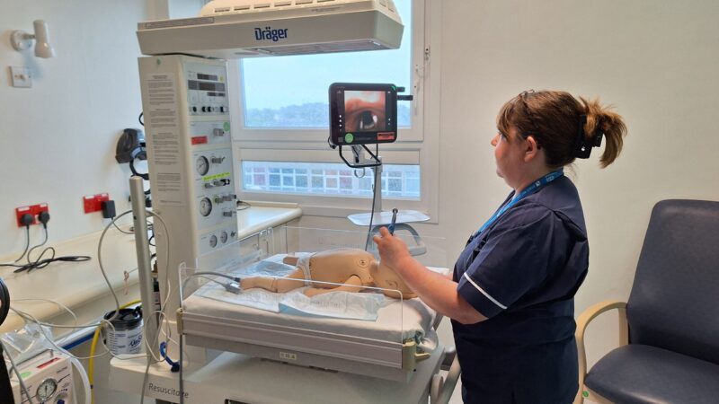 Clare Easson demonstrates the GlideScope. She holds the small camera in an infant manikin's mouth. The screen shows the manikin's airway.