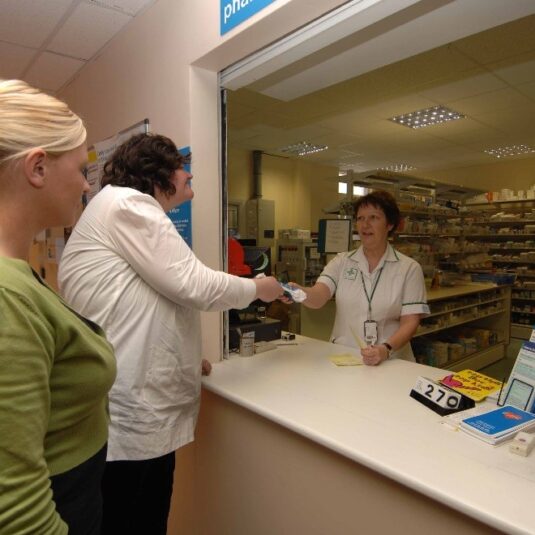 Patient with their carer collects medicine from pharmacy hatch.
