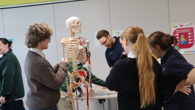 Staff talk to a teenage girl. A member of staff points at a skeleton.