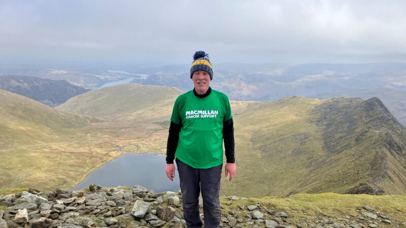 Man stands at top of mountain after cancer treatment.