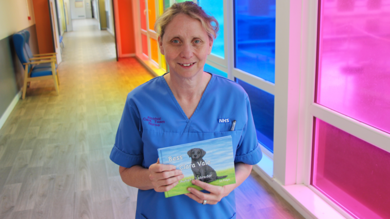 Lin Fidgin holds a copy of the book. On the front cover is a black dog sitting down on grass.