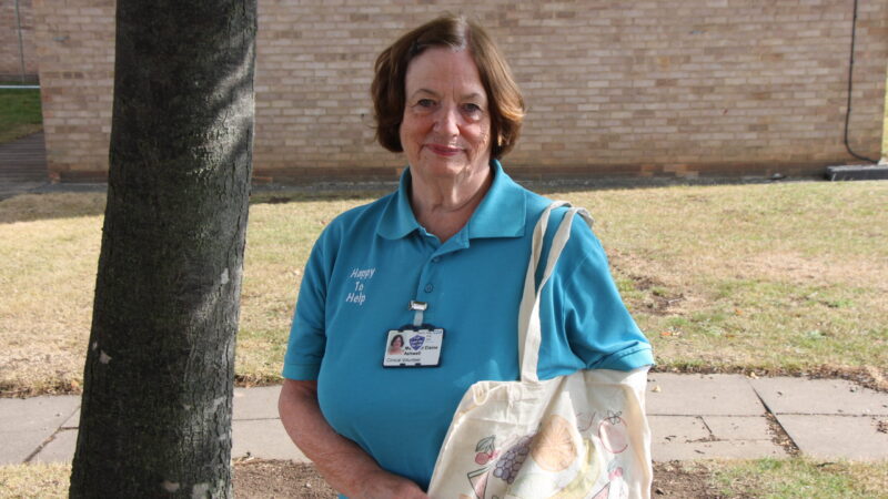 A volunteer carries a tote bag. The bag features an illustrated drawing of various fruit and vegetables.