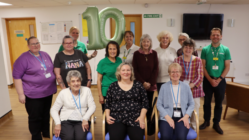 Members of the group. They hold large green balloons spelling out '10'.