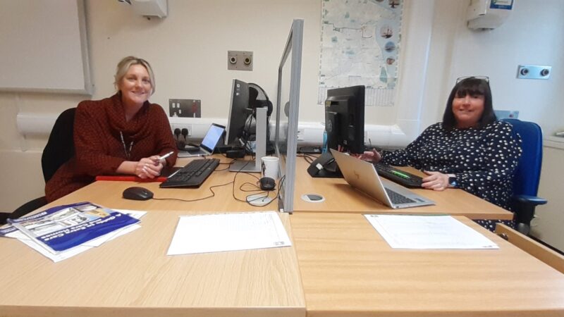 Karen Flounders and Angie Caswell sit at their desks in front of PCs.