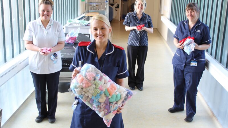 Staff stand in a corridor. They hold knitted love hearts.