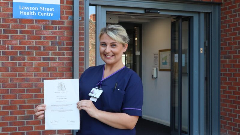 District nurse stood in front of health centre with certificate