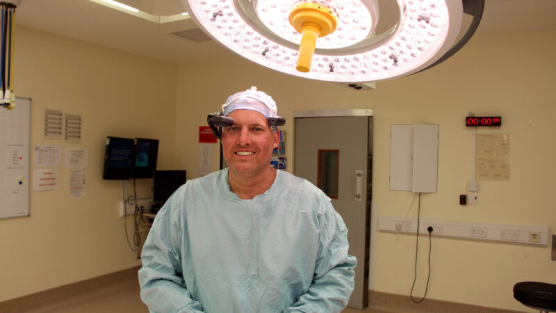 Nick Cooke stands in an operating theatre. He wears scrubs and a camera headset.
