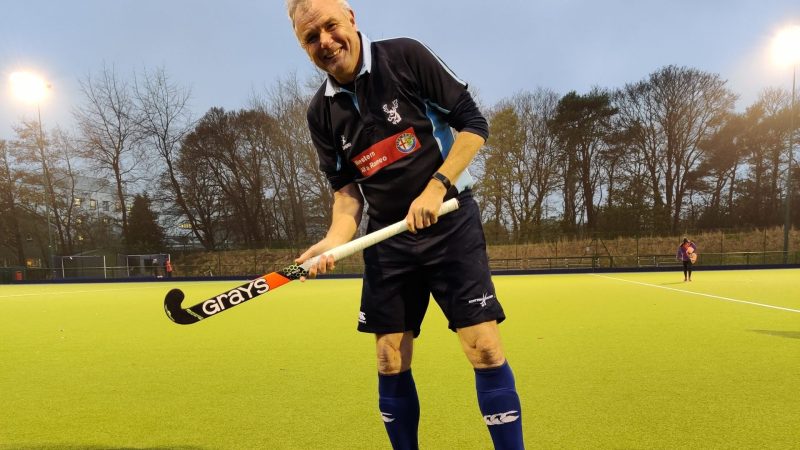 Derek Bell holding a hockey stick on a hockey pitch.