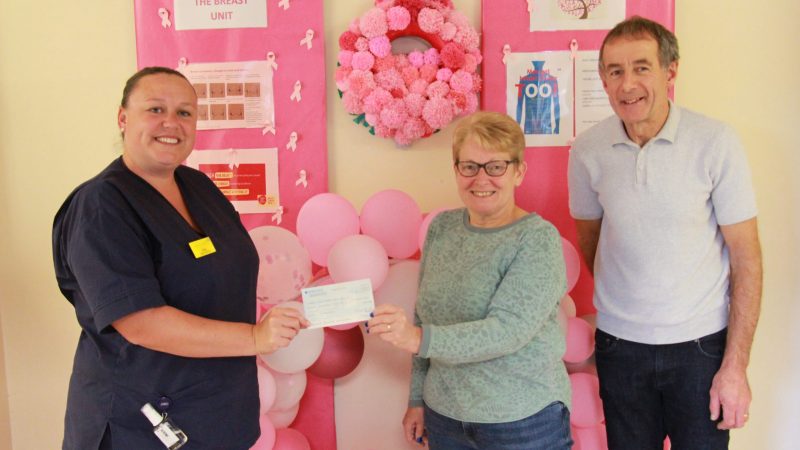 Rosanne and Craig in the breast unit. Rosanne is handing a cheque to breast care nurse Vicky Hay.