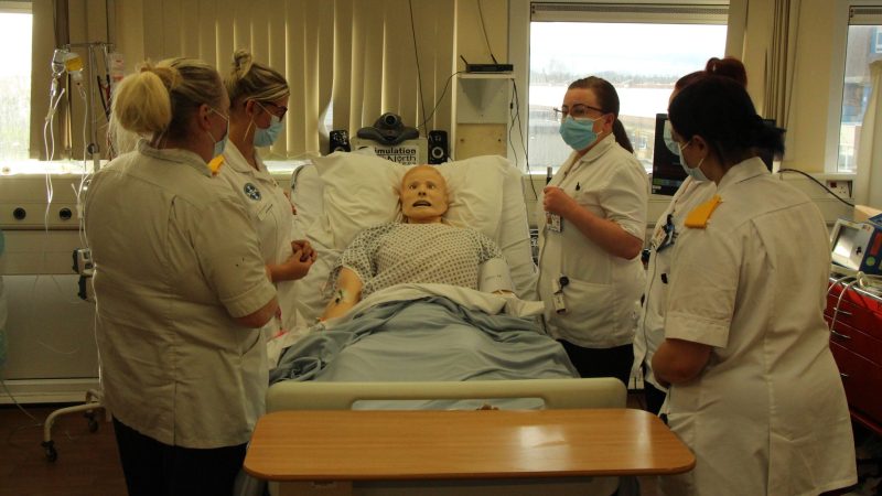Nurses stood around a simulation model in bed.