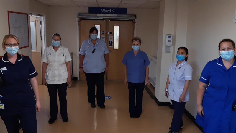 The Hartlepool elective care team. They stand in the corridor outside ward 9. They all wear face masks.