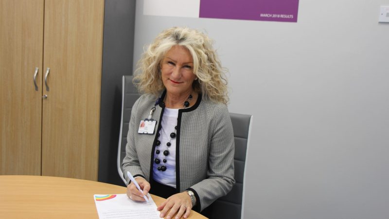 Julie Gillon sits at a desk. She is signing her signature on the letter,