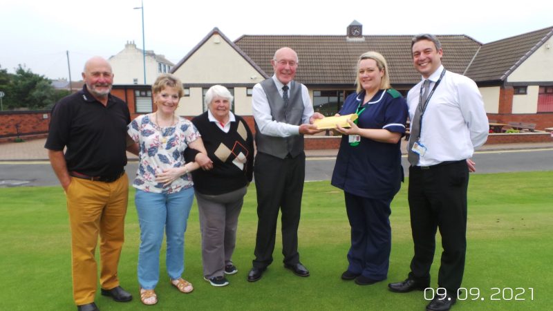 Helen and Dicken and Richard Scott with Ian Phillips and members of the golf club. Ian hands an envelope to Helen.