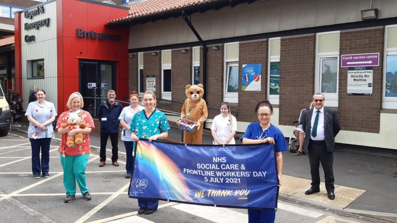 Staff with members of the Freemasons. One is dressed up as a teddy bear. Two members of staff hold a banner reading: "NHS social care and frontline workers' day 5 July 2021. We thank you."